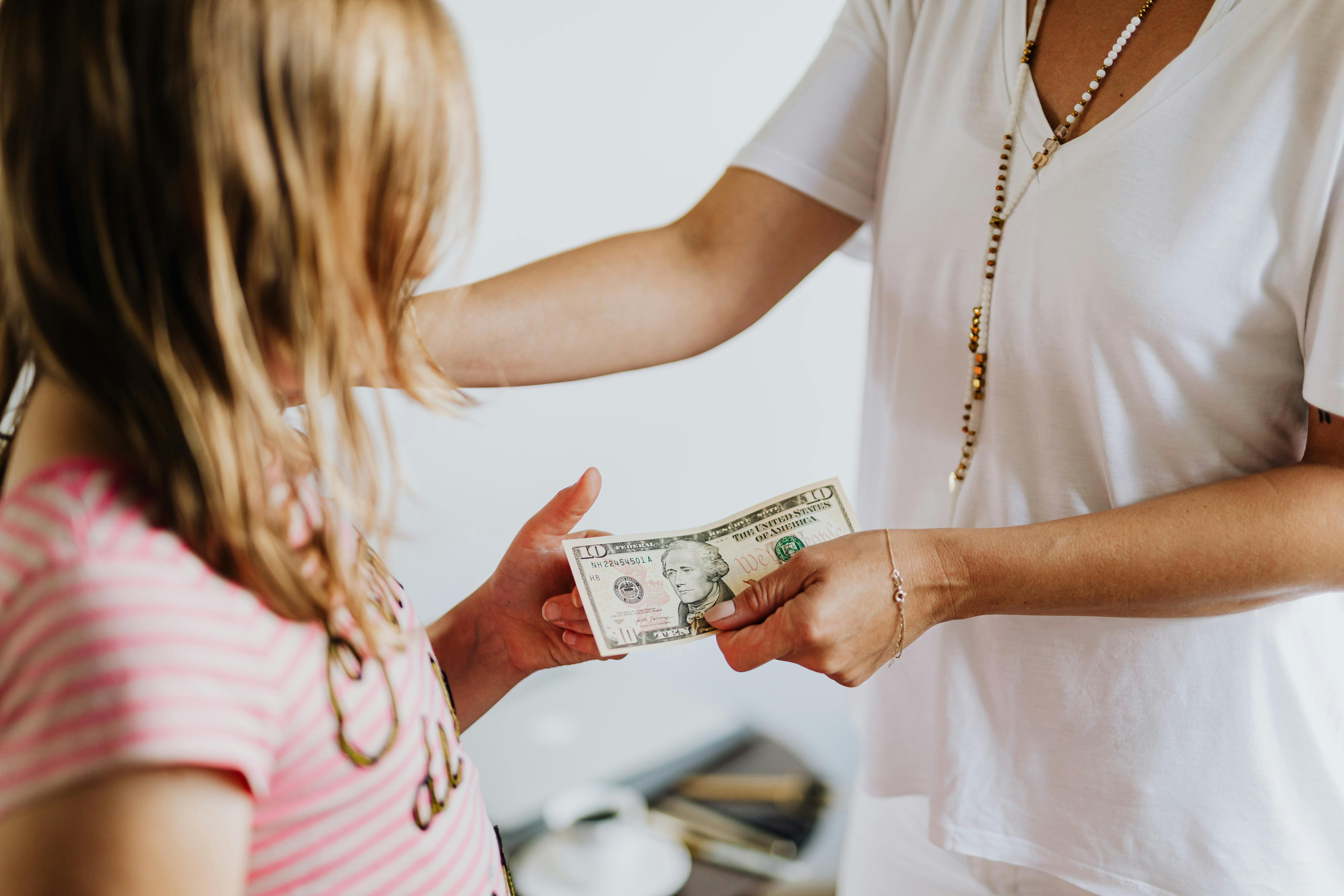 An Adult Giving a Ten-Dollar Bill to a Child