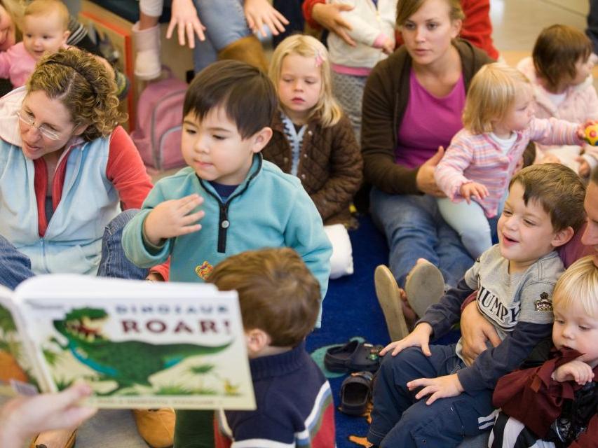 Children and Adults Sitting Listening to a book called Dinosaur Roar