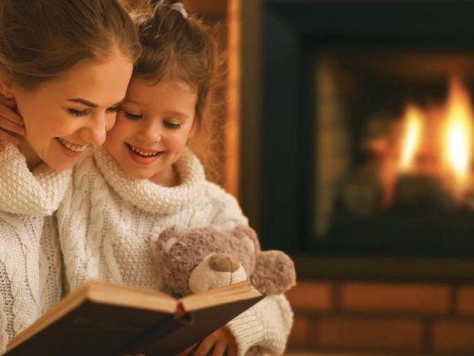 Mother and Child In Sweaters reading a book with a fireplace in the Background
