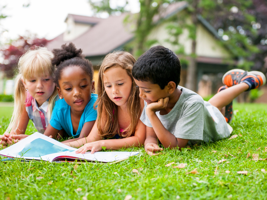 Children reading a book together outside